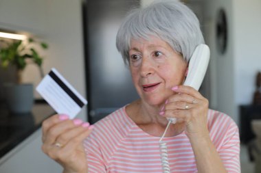 Telefon görüşmesi sırasında kredi kartı tutan şüpheli görünen son sınıf öğrencisi bir kadın.