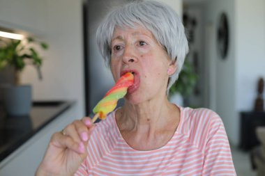 Senior woman eating a popsicle at home clipart