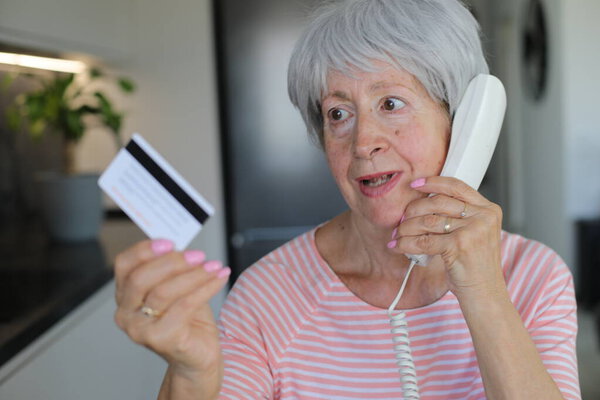 Skeptical looking senior woman holding credit card during phone call