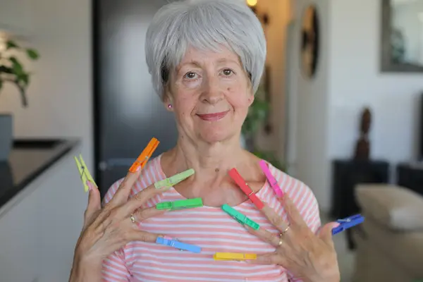 stock image Senior woman pretending to have long nails with clothespins