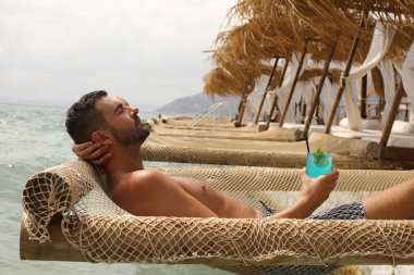 Yakışıklı adam askıdaki ağa uzanmış kokteyl içiyor.