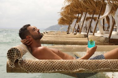 Yakışıklı adam askıdaki ağa uzanmış kokteyl içiyor.