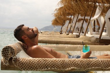 Yakışıklı adam askıdaki ağa uzanmış kokteyl içiyor.