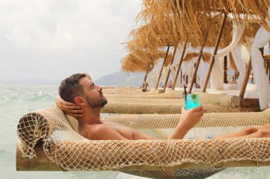 Yakışıklı adam askıdaki ağa uzanmış kokteyl içiyor.