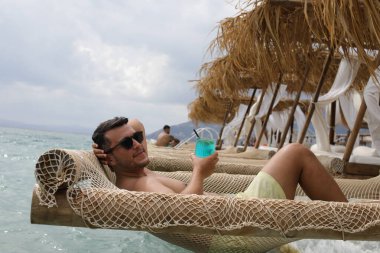 Yakışıklı adam askıdaki ağa uzanmış kokteyl içiyor.