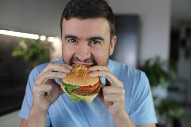 Evde hamburger yiyen yakışıklı bir adam.