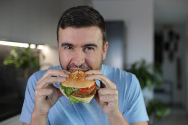Evde hamburger yiyen yakışıklı bir adam.