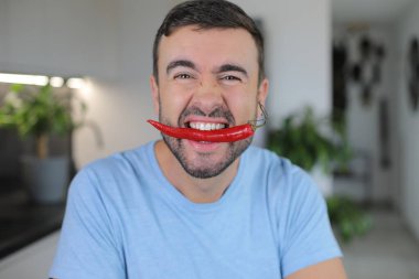 Man holding in his mouth, a very spicy ingredient clipart