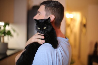 Yakışıklı adam kara kedi tutuyor.