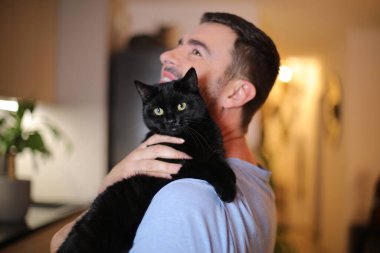 Yakışıklı adam kara kedi tutuyor.
