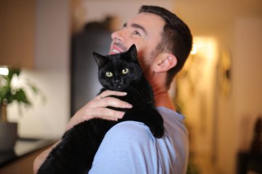 Yakışıklı adam kara kedi tutuyor.