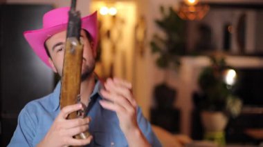Yakışıklı, gururlu, pembe şapkalı ve klasik silahını gösteren bir kovboy. 