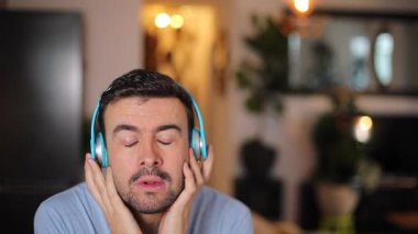 Yakışıklı adam kulaklıklarıyla müzik dinliyor ve evde dans ediyor.