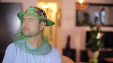 Evde sivrisinek karşıtı özel bir şapka takan komik bir adam.