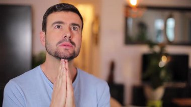 Genç adam bir oturma odasında dua ediyor.