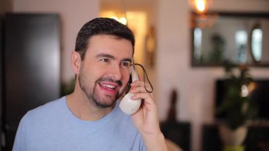 Yakışıklı adam evde, oturma odasında telefonla konuşuyor.