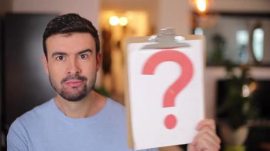 Evdeki oturma odasında üzerinde soru işareti olan boş bir tabela tutan adam.