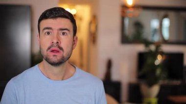 Şaşırmış bir adam evdeki oturma odasında kameraya bakıyor.