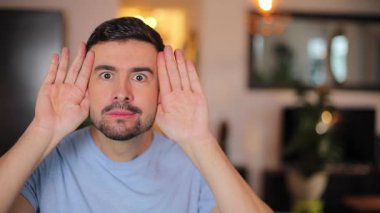 Evdeki oturma odasında el kol hareketi yapan genç adam.