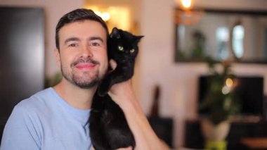 Yakışıklı genç adam küçük siyah bir kedi tutuyor.