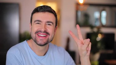 Genç, yakışıklı, orta yaşlı adamın portresi evde barış işareti gösteriyor.