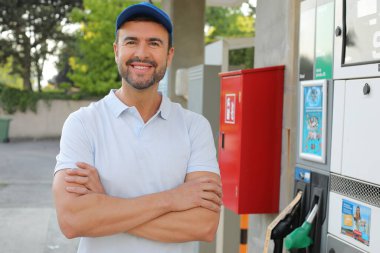 Genç yakışıklı adam gülümsüyor, istasyonda araba pompası tutuyor.