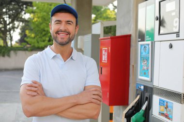 Genç yakışıklı adam gülümsüyor, istasyonda araba pompası tutuyor.