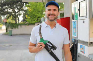 Genç yakışıklı adam gülümsüyor, istasyonda araba pompası tutuyor.