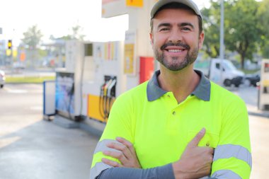 Mutlu gülüşü ve kendine güveni olan genç yakışıklı adam şehirde benzin istasyonunda duruyor.
