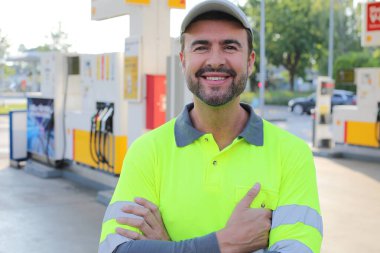 Mutlu gülüşü ve kendine güveni olan genç yakışıklı adam şehirde benzin istasyonunda duruyor.