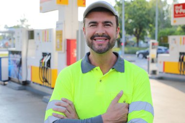Mutlu gülüşü ve kendine güveni olan genç yakışıklı adam şehirde benzin istasyonunda duruyor.