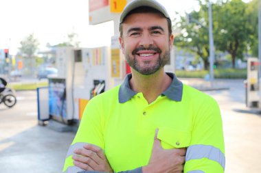 Mutlu gülüşü ve kendine güveni olan genç yakışıklı adam şehirde benzin istasyonunda duruyor.