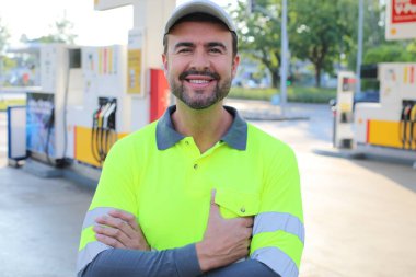 Mutlu gülüşü ve kendine güveni olan genç yakışıklı adam şehirde benzin istasyonunda duruyor.