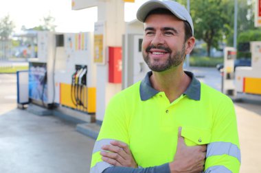 Mutlu gülüşü ve kendine güveni olan genç yakışıklı adam şehirde benzin istasyonunda duruyor.