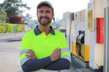 Mutlu gülüşü ve kendine güveni olan genç yakışıklı adam şehirde benzin istasyonunda duruyor.