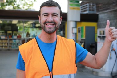 Güvenlik yeleği giyen ve baş parmağını kaldıran genç bir adam.