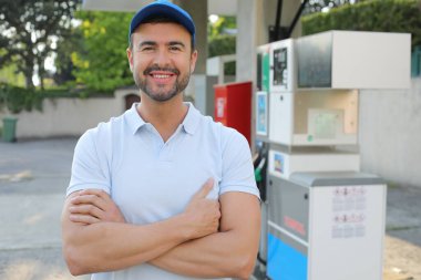 Mutlu gülümseyen erkek işçi benzin istasyonunun yanında duruyor.