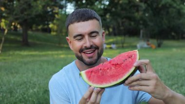 Yeşil çimlerde karpuz yiyen yakışıklı adam.