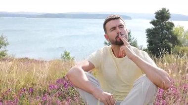 Genç adam, gölün kenarında elinde çiçeklerle sigara içiyor.
