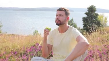 Göl kenarında elma yiyen mutlu genç adamın portresi.