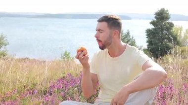Göl kenarında elma yiyen mutlu genç adamın portresi.