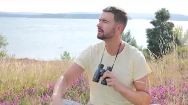 Yazın göl kenarında siyah dürbünlü bir adam oturuyor.