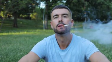 Genç adam parkta sigara içiyor.