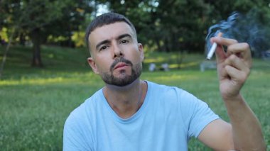 Genç adam parkta sigara içiyor.
