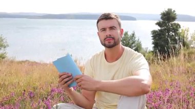 Yazın göl kenarında defter okuyan yakışıklı adam.