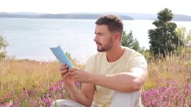 Yazın göl kenarında defter okuyan yakışıklı adam.