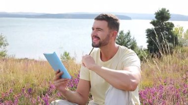 Yazın göl kenarında defter okuyan yakışıklı adam.