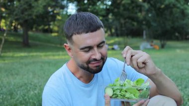 Dışarıda yeşil salata yiyen bir adamın portresi.