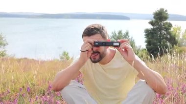 Gölün ve çiçeklerin arka planında kamerası olan yakışıklı bir fotoğrafçı.