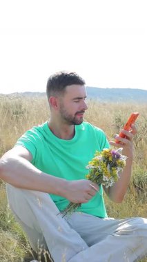 Akıllı telefonu ve elinde çiçekleri olan genç bir adam.